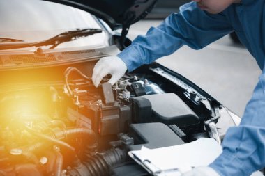 Bir atölyede otomobil teknisyeni, bir not panosuna yazı yazıyor. Araç motorlarını kontrol ediyor. Güvenlik ve bakım üzerine odaklanan mekanik uzmanlığı. Otomotiv sektöründe iş çalışırken gülümsüyor.