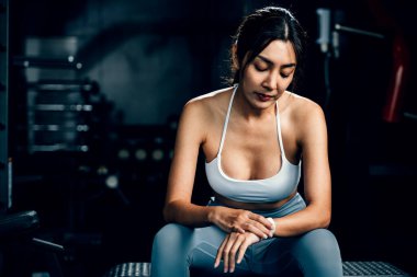 Asyalı kadın yedek kulübesinde dinleniyor ve beden eğitimi aldıktan sonra tüm güncellemeleri kontrol ediyor. Kadın spor salonunda spor yaparken akıllı saat kullanıyor. Sağlıklı yaşam tarzı konsepti.