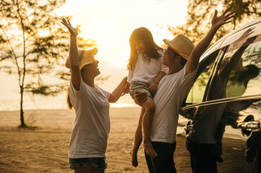 Asyalı aile gün batımında araba vitrininde oynarken tatillerde ve dinlenirken tuhaf hissediyorlar. İyi hafta sonları. Plajda iyi tatiller. Yaz tatili yolculuk konsepti