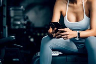 Asyalı kadın yedek kulübesinde dinleniyor ve beden eğitimi aldıktan sonra tüm güncellemeleri kontrol ediyor. Kadın spor salonunda spor yaparken cep telefonu uygulaması kullanıyor. Sağlıklı yaşam tarzı konsepti.