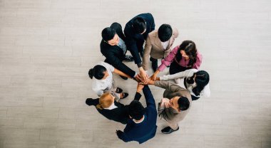 Yukarıdan, çeşitli iş adamlarından oluşan bir dörtlü, sembolik bir yığın oluşturmak için el ele tutuşuyor. Bu resim birlik takım çalışmasını ve küresel işbirliğini temsil ediyor.