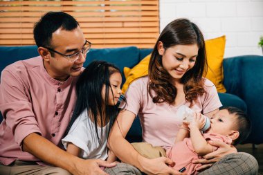 Bir anne, yeni doğmuş bebeğini oturma odasında bir şişeyle beslerken küçük oğlu ve kızı da babasıyla geçirdiği anın tadını çıkarıyor. Evlerinde sevgi ve birliktelik mutluluğun odak noktasıdır..