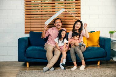 Çocuklarını seven bir anne ve baba yeni evlerindeki kanepede ellerinde karton bir çatı modeliyle gülümsüyor. Eve taşınma sırasında güvenlik ve birliktelik mutluluğun anahtarıdır..