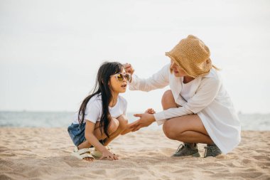 Gün batımında sahilde aile eğlencesi. Anne ve kızı kumda oturuyor. Karayipler 'deki tatil ortamı mutluluk ve neşe ile doludur. Kaygısız bir bağ anı