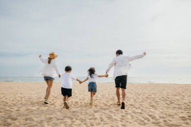 Mutlu ebeveynler plajda çocuklarıyla el ele koşup neşeyle zıplıyorlar. Sahil tatilinin özünü yansıtan yürek ısıtan bir aile birlikteliği ve tasasız bir eğlence sahnesi..