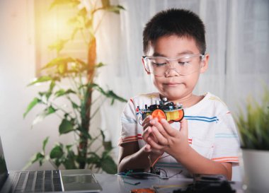 Küçük çocuk oyuncakları birleştirmeye çalışıyor, Asyalı çocuk Arduino robot araba ödevinde tekerlek birleştiriyor, elektronik yapay zeka atölyesi çevrimiçi okul dersi yaratıyor.