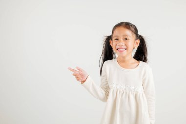 Mutlu Asya portresi gülümseyen küçük kız parmak boşluğunu gösteriyor, stüdyo resmi beyaz arka planda izole edilmiş, Tayland anaokulu çocuğu kopya alanı ile işaret ediyor.