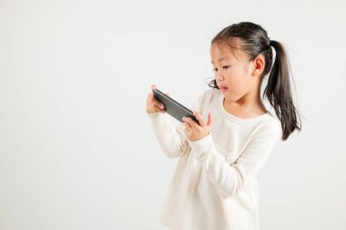 Beyaz arka planda izole edilmiş akıllı cep telefonu stüdyosunu kullanarak heyecanla gülümseyen mutlu Asyalı genç kız portresi.