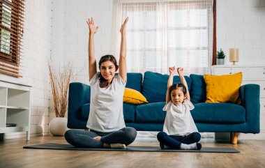 Sıcak evlerinde bir anne ve tatlı kızı yoga yapıyorlar. Aile yogası yapıyorlar. Esneyip denge kurarken gülümsüyorlar..