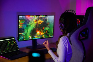 Asyalı oyuncu online video oyunu oynuyor masaüstü bilgisayar ekranında heyecan verici neon LED ışıklar, oyun kulaklıklı kadın mutlu bilgisayar kullanıyor, muhtemelen zaferi kutluyor, E-Sport