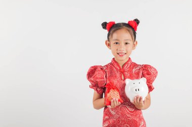 Kırmızı Cheongsam elbiseli gülümseyen Asyalı mutlu bir Çin Yeni Yılı kızı elinde bir kumbara ve kırmızı para çantası tutuyor. Beyaz arka planda izole edilmiş, birikimleri, refahı ve festival geleneklerini sembolize ediyor..