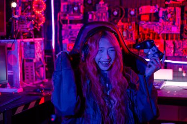 Kazanmak. Happy Gamer sanal turnuva için oyun kumandası kullanıyor bilgisayarla online video oyunu oynuyor kutlama yapmak için elini kaldırıyor oyun kulaklığı takan Asyalı kadın heyecanlanıyor