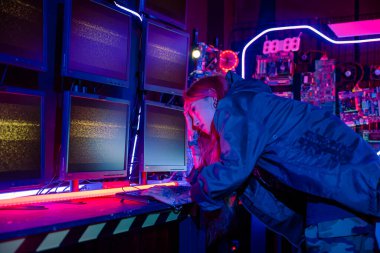 Siyah ceketli Asyalı bir kadın bilgisayar programlama sistemini hackliyor ve karanlık ofiste bilgisayar monitörüyle çalışıyor. Siber güvenlik sitesi geliştirme, siber güvenlik, bilgi izleme...