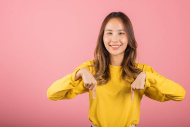 Asyalı mutlu bir portre gülümseyen güzel bir genç kadın, iki parmağını aşağıdan işaret ediyor sunuyor ve bakıyor, pembe arka planda izole edilmiş, fotokopi çekiliyor, aşağıya bakıyor.