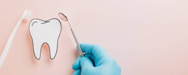 Diş fırçası, diş fırçası ve pembe eldivenli bir el tarafından tutulan ayna. Dişçi Günü konsepti, düz bir dizaynda diş hijyeni, ağız sağlığı kontrolü ve tıbbi bakımı vurguluyor..