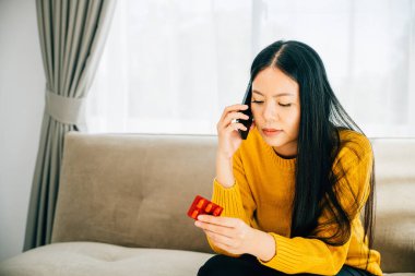 Ev danışmanlığı, kanepede yatan hasta Asyalı kadın telefonla doktorlara danışmanlık yapıyor. Koronavirüsün ortasında tıbbi bakım karantinası ve sosyal mesafeyi yansıtıyor..