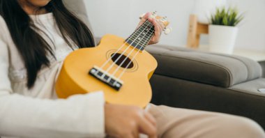 Genç kız rahat bir kanepede gitar çalıyor. Tellerin üzerindeki ellerinin detaylı görüntüsü müziğe olan sevgisini gösteriyor. Modern, hafif aydınlatılmış bir oturma odasında geçiyor..
