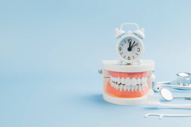 Dişçi günü. Bir dişçi diş bakımını ve ağız sağlığını geliştirmek için mavi arka planda bir diş modeli, steteskop, aletler ve beyaz alarmlı bir saat düzenler..