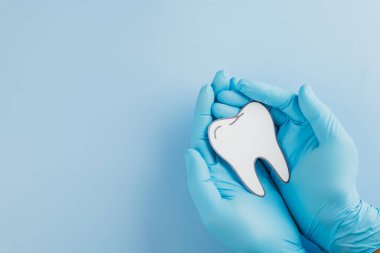 Diş Hekimi Günü, dişçi eldivenli eller, diş sağlığı, tıbbi farkındalık ve diş hekimlerinin sözlü bakımdaki önemini vurgulayan bir diş kağıdı kesiğini nazikçe tutarlar. Boşluğu kopyala, üst görünüm