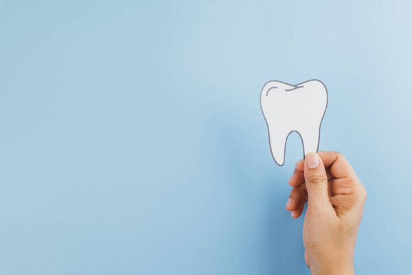 Dentist Day, a woman hands firmly hold a tooth paper cutout, highlighting dentistry, oral health, and the crucial role of dentists in medical care. copy space, top view