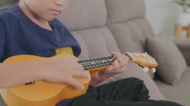 Gülümseyen çocuk gri bir kanepeye oturur, gitar çalar. Telleri çalarken yakın plan çekimleri, rahat bir oturma odasında müzik zevkini yakalamak..