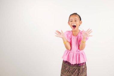 Taylandlı genç kızın geleneksel Tayland elbisesi gülümsemesi başarısını kutlamak için yumruklarını kaldırıyor, stüdyo izole edilmiş beyaz arka plan, anaokulu çocuğu heyecanla evet diyor.