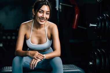 Asyalı kadın yedek kulübesinde dinleniyor ve beden eğitimi aldıktan sonra tüm güncellemeleri kontrol ediyor. Kadın spor salonunda spor yaparken akıllı saat kullanıyor. Sağlıklı yaşam tarzı konsepti.