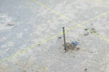 Tabanda kesişen sert beton ve sarı çizgilere gömülü bir çivinin yakın çekimi, inşaat ve seramik projeleri için doğruluğu gösteriyor.