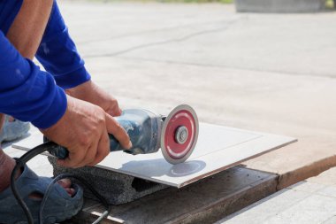 Hassasiyet ve uzmanlık: Mavi elbiseli bir işçi inşaat sahasında gri bir fayans oluşturmak için bir açı öğütücü kullanır, detaylara ve işçiliğe özen gösterir.