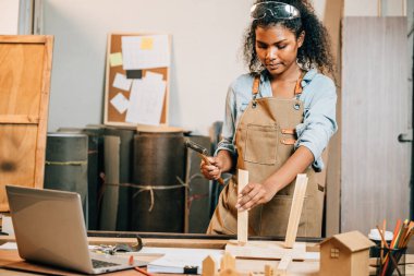 Afro-Amerikalı marangoz kadın bir marangoz dükkanında bir sandalye için bir tahta parçasını çekiçliyor. Ahşap mobilya ustalığı, atölyede zanaat, DIY, Ulusal Marangozlar Günü