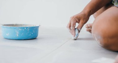 Döşeme işleminin yakın çekimi: Gri zemin fayanslarının üzerinde kauçuk bir yüzgeçle elle yumuşatıcı harç. Temiz dikişlere ve hatta uygulamaya dikkat edin.