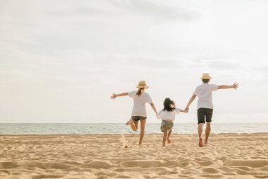 Mutlu Asyalı ebeveynler ve kızları sahilde eğleniyorlar. Kumda koşan ve rol yapan anne ve babalarıyla küçük kızlar. Olumlu aile aktivitesi