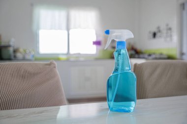 Beyaz masa üstünde temiz sıvı bulunan mavi sprey şişesi bulanık arkaplan odaklı. Temizlik aletlerini temsil ediyor. Mutfaktaki cam sprey şişesi modern temizlik konseptini ön plana çıkarıyor.