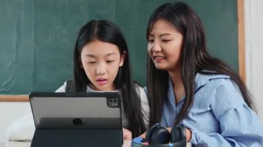 Bir kadın ve bir kız önlerinde bir tabletle bir masada oturuyorlar. Tablet, öğrenme, eğlence gibi çeşitli amaçlar için kullanılabilen akıllı bir araçtır.