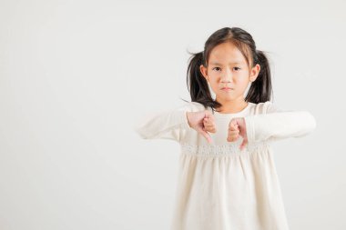 Morali bozuk Asyalı genç bir kızın portresi, hoşnutsuzluğu sembolize eden bir jest sergiliyor. Stüdyo görüntüsü beyaz, fotokopi alanı var, anaokulu çocuğu negatif ve üzgün bir görünüm sergiliyor.