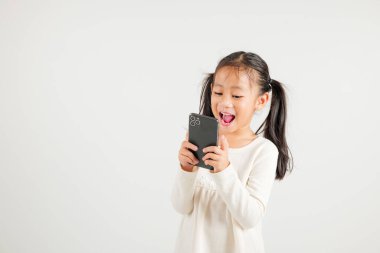 Beyaz arka planda izole edilmiş akıllı cep telefonu stüdyosunu kullanarak heyecanla gülümseyen mutlu Asyalı genç kız portresi.