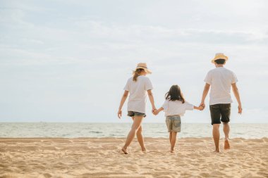 Mutlu Asyalı ebeveynler ve kızları sahilde eğleniyorlar. Anne ve babalarıyla birlikte kumsalda yürüyen bir çocuğun elini tutan küçük kızlar. Olumlu aile aktivitesi