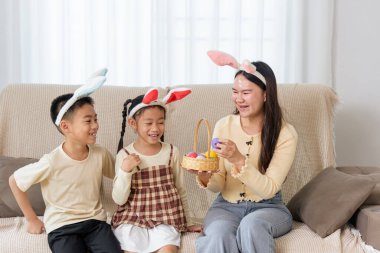 Paskalya aile zamanı. Tavşan kulaklı mutlu çocuklar ve anneleri ellerinde bir sepet Paskalya yumurtası tutarken gülümseyerek sıcak bir evde tatilin tadını çıkarıyorlar..