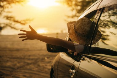 Şık şapkalı bir kadın gün batımında el sallayarak arabanın ön koltuğunda oturur ve rüzgarı hisseder. İyi hafta sonları. Plajda iyi tatiller. Yolculuk ve özgürlük kavramı
