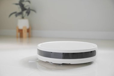 Ön siyah sensör şeritli, fayans zemininde yan fırçası olan beyaz otomatik yer temizleyicisi. Robot elektrikli süpürge zemini etkin bir şekilde temizliyor, toz temizleme için akıllı ev teknolojisini gösteriyor