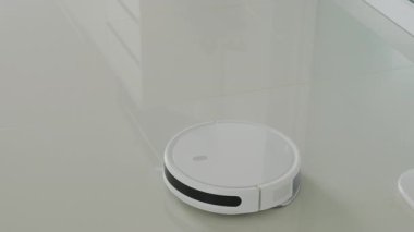 Fayans döşeme üzerinde yan fırçası olan beyaz otomatik yer temizleyicisi, verimli temizlik için tasarlanmış. Robot vakum konsepti. Akıllı ev teknolojisi. Çeşitli yüzeylerin sorunsuz, kablosuz temizlenmesi için.