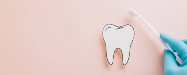 Kağıt diş ve eldivenli el, pastel pembede diş fırçasını tutuyor. Yaratıcı bir dairede sağlık, tıbbi bakım ve ağız sağlığını kutlayan bir dişçi günü tasarımı.