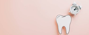 Dişçi Günü farkındalığı. Kağıt diş ve pembe arka planda beyaz alarm saati. Dünya Ağız Sağlığı Günü 