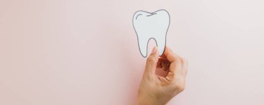 Dişçi günü. Kadın elleri pembe arka planda bir diş kâğıdı tutuyor, diş sağlığı ve ağız temizliğini sembolize eden bir dişçi..