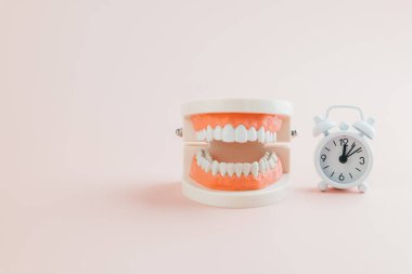 Diş Hekimleri Günü hatırlatıcısı. Pembe arka plandaki beyaz alarm saati ve diş modeli, dişçi bakımını, ağız sağlığını ve Dünya Ağız Sağlığı Günü için diş bilincini vurgulamaktadır..