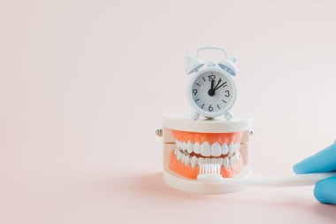Diş hekiminin diş fırçasıyla diş fırçasını fırçalarken diş hekimi, diş hekimi Günü ve Dünya Ağız Sağlığı Günü 'nü hatırlatmak için beyaz bir çalar saat sergiliyor..