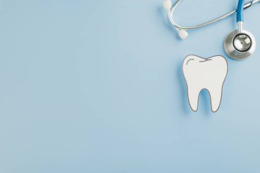 Kağıt kesiği diş ve steteskop mavi arka planda dişçi gününü sembolize ediyor. Tüm dünyada diş hekimlerini, diş bakımını ve oral sağlık bilincini kutlayın. Kopyalama alanı olan üst görünüm