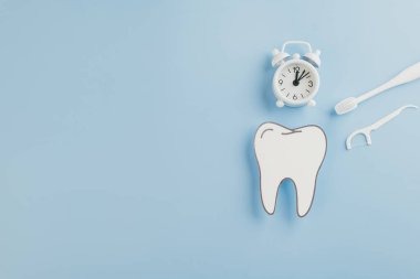 Dişçi günü konsepti. Kağıt diş, diş aletleri ve mavi arka planda beyaz saat diş hekimi hatırlatıcıları, ağız bakımı ve Dünya Ağız Sağlığı Günü farkındalığı. Düz yatış, Üst Görünüm