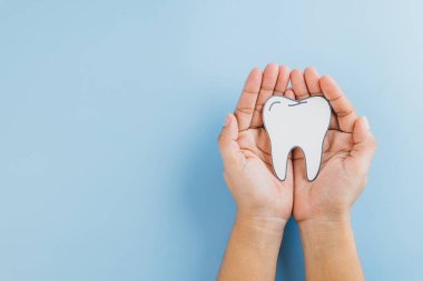 Dişçi günü konsepti. Bir kadın elinde mavi, diş hekimliğinin altını çizen, ağız sağlığı ve tıbbi bakımdaki dişçilerin rolü ile ilgili bir diş kağıdı var. Düz yatış, Üst Görünüm