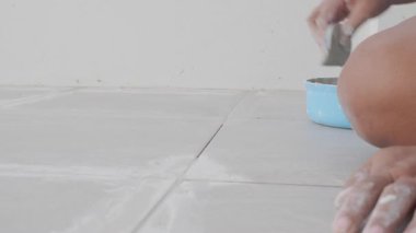 Gri seramik döşemeler arasında havan topu düzleştiren lastik malalı bir el. Döşeme işi sırasında hassas ve temiz dikişler için ayrıştırma sürecinin yakın plan görüntüsü.